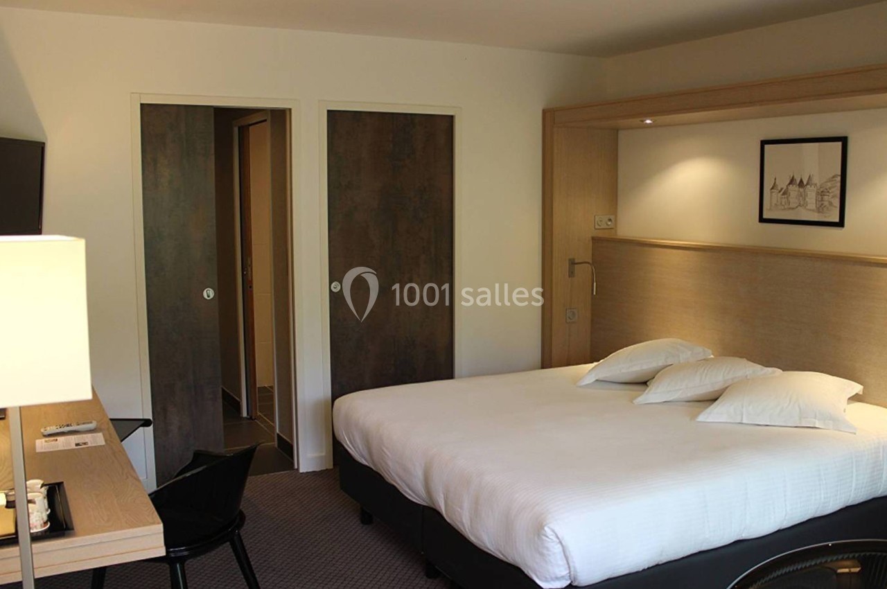 Chambre d'hôtel avec lit double, bureau équipé, télévision murale et portes menant à une salle de bain.