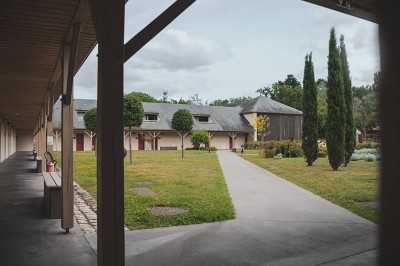 Salon d'hôtel avec canapés beiges, table basse, bureau, chaise noire et grande baie vitrée donnant sur un jardin.