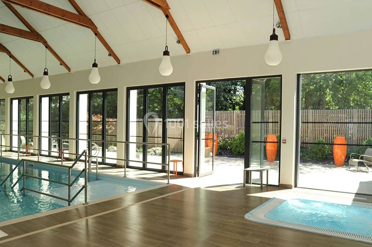 Piscine intérieure lumineuse avec grandes baies vitrées ouvertes sur une terrasse et un espace extérieur verdoyant.