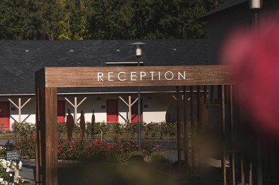 Salon d'hôtel avec canapés beiges, table basse, bureau, chaise noire et grande baie vitrée donnant sur un jardin.