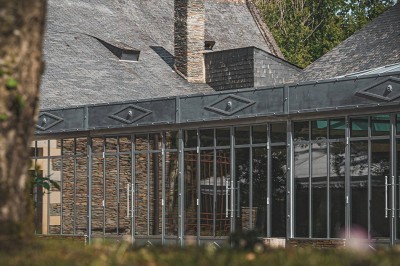 Salon d'hôtel avec canapés beiges, table basse, bureau, chaise noire et grande baie vitrée donnant sur un jardin.