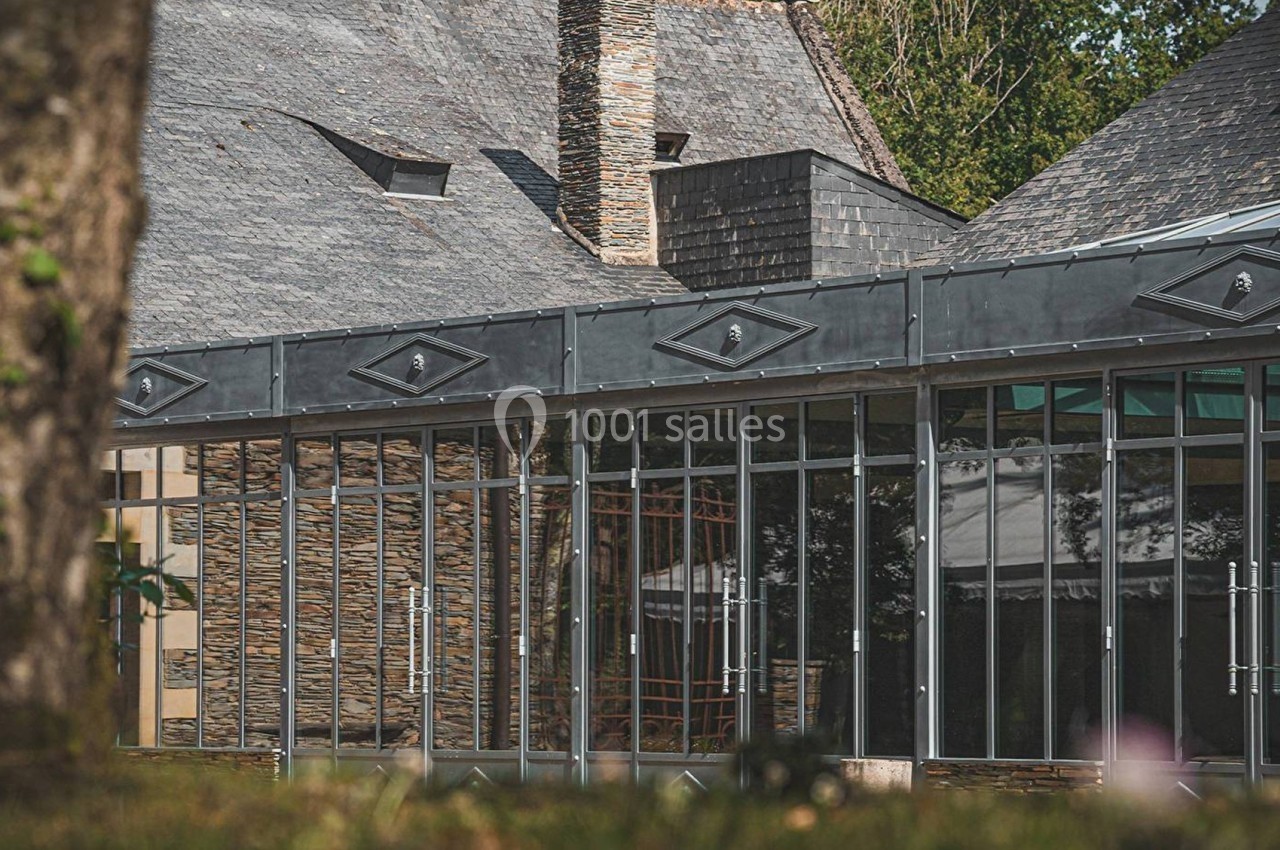 Façade vitrée d'un bâtiment moderne avec toit en ardoise, entouré de verdure.