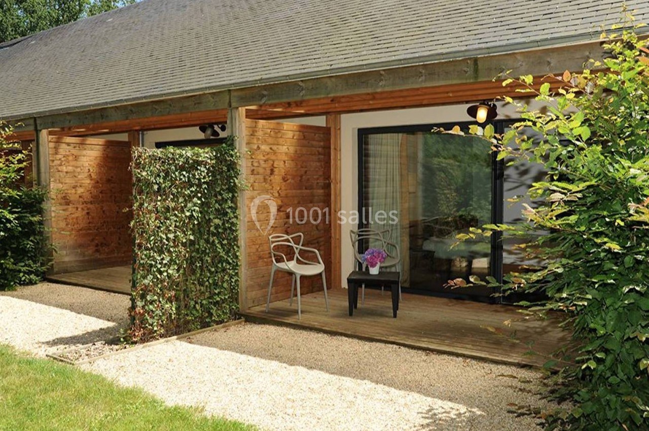 Terrasse en bois devant une maison avec bardage en bois, séparée par un panneau végétal, entourée de verdure.