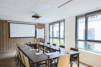 Salle de conférence moderne avec rangées de sièges en bois et éclairage suspendu.