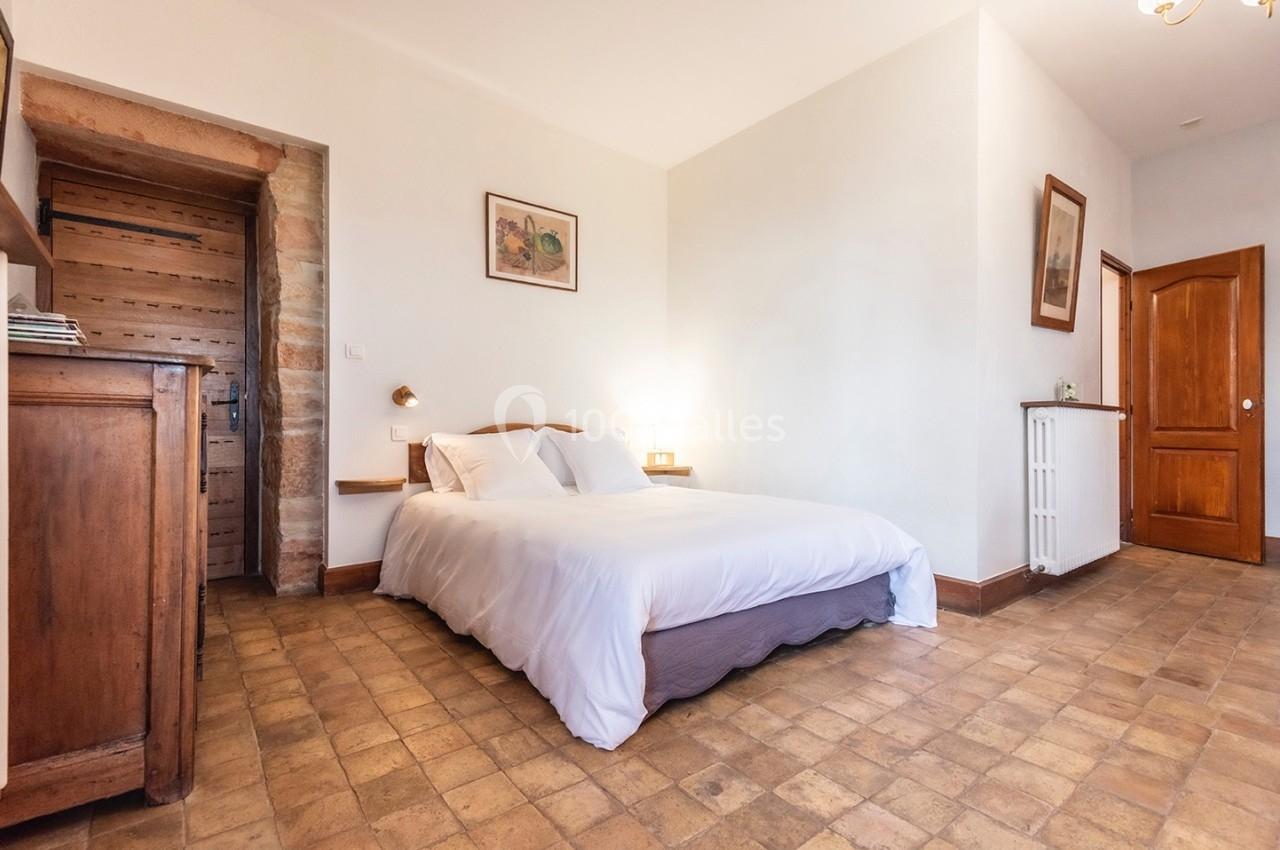 Chambre lumineuse avec lit double, sol en carreaux de terre cuite, mobilier en bois et porte en bois massif.