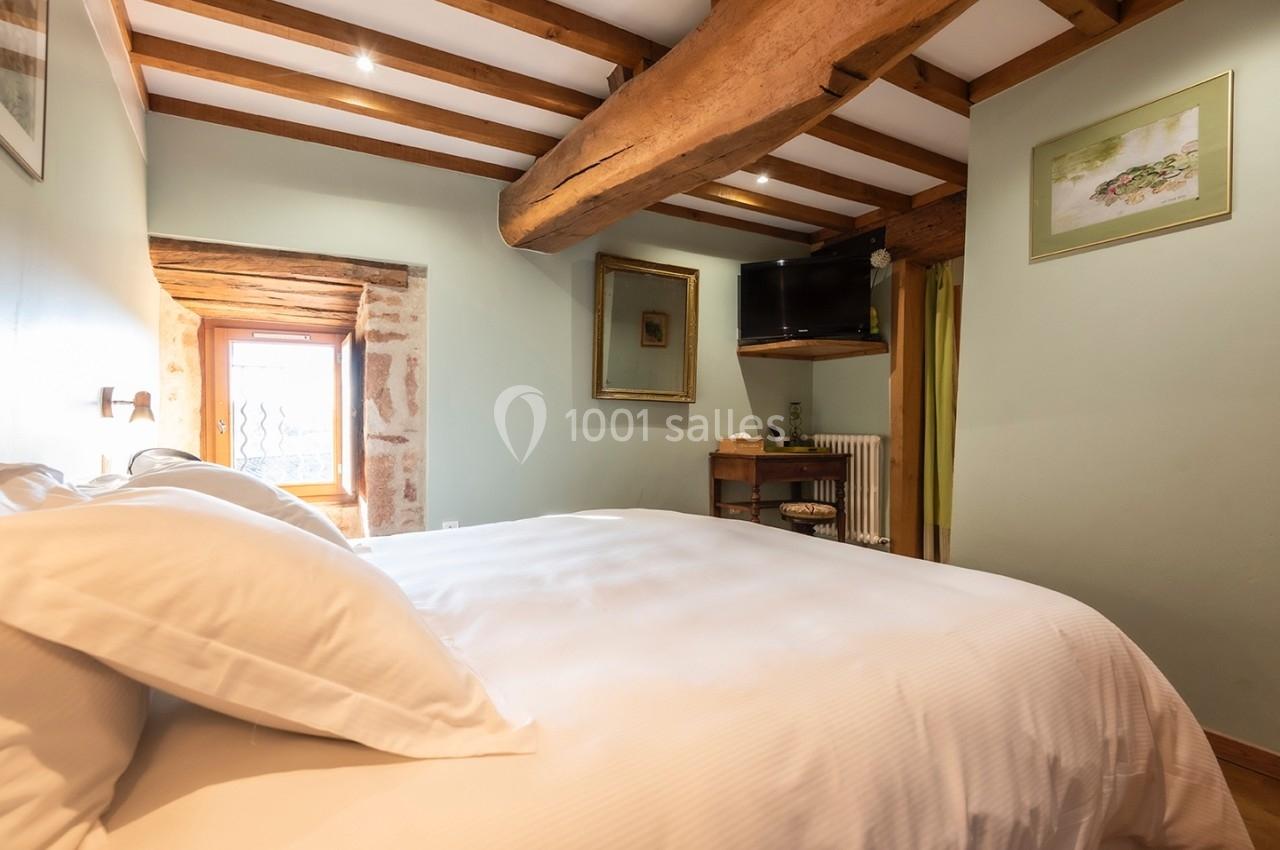 Chambre lumineuse avec poutres apparentes, lit double, murs pastel, télévision et fenêtre donnant sur l'extérieur.