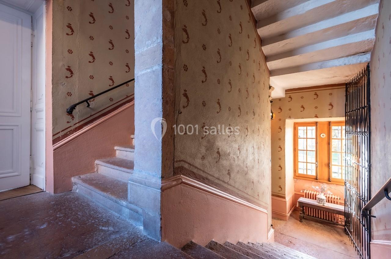 Escalier intérieur ancien avec murs ornés de motifs, rampe en métal et lumière naturelle entrant par une fenêtre.