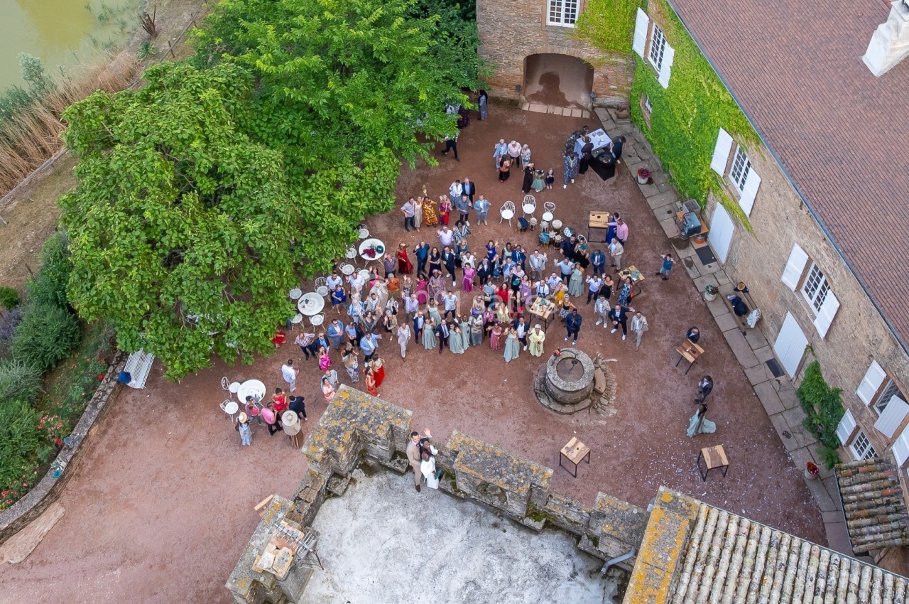 Vue aérienne d'un rassemblement de personnes dans la cour d'un bâtiment ancien entouré de végétation.