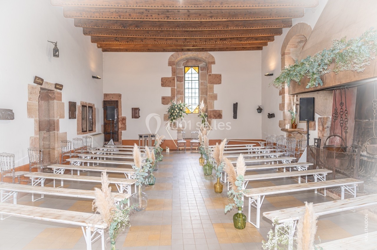 Salle de cérémonie lumineuse avec bancs en bois, décorations florales et vitrail coloré au fond.
