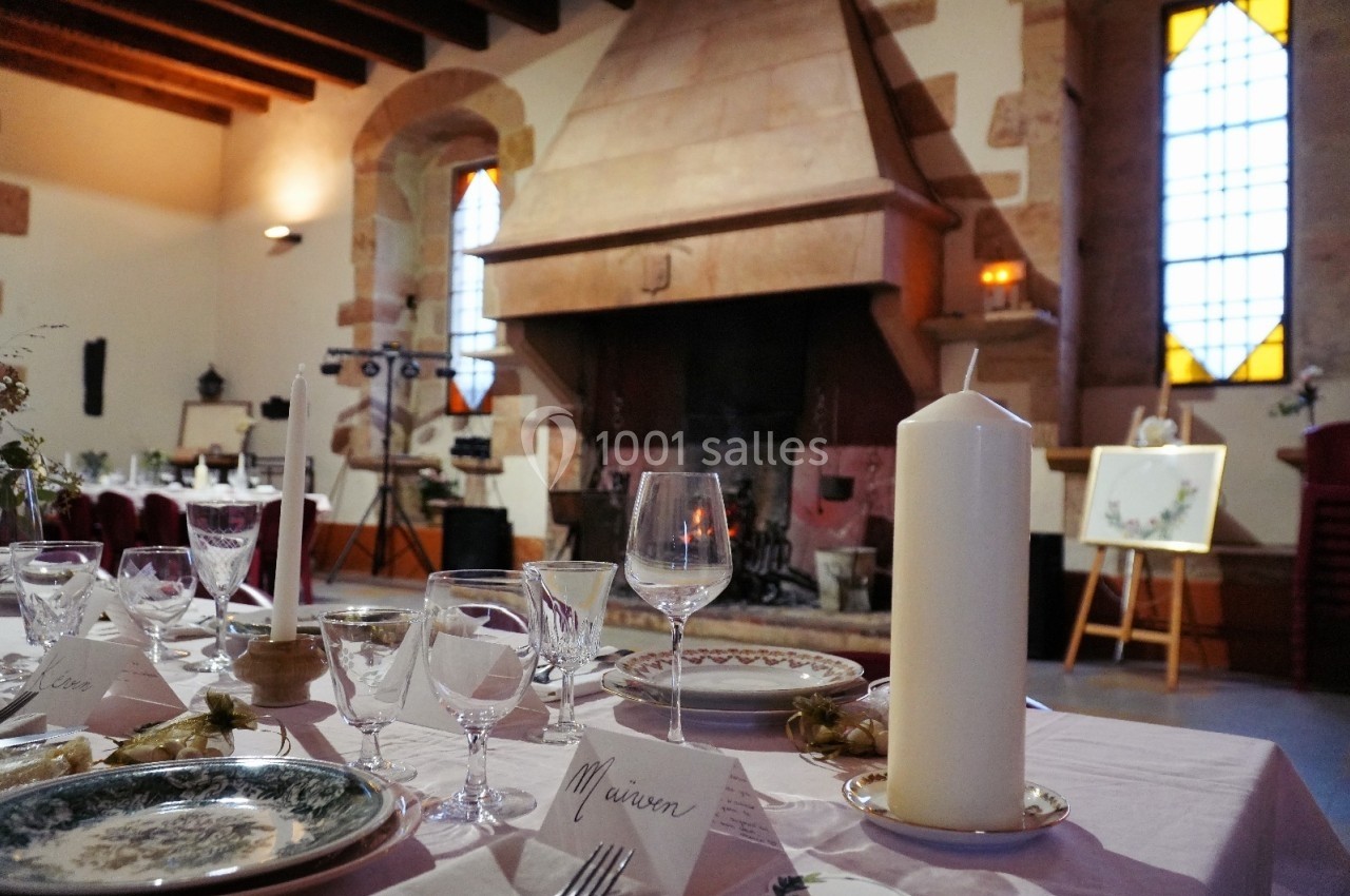 Table dressée pour un événement dans une salle avec cheminée en pierre, vitraux colorés et décorations élégantes.