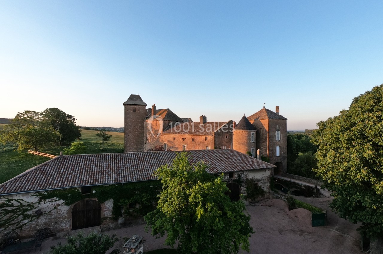Vue d'un château en pierre entouré de verdure sous un ciel dégagé au coucher du soleil.