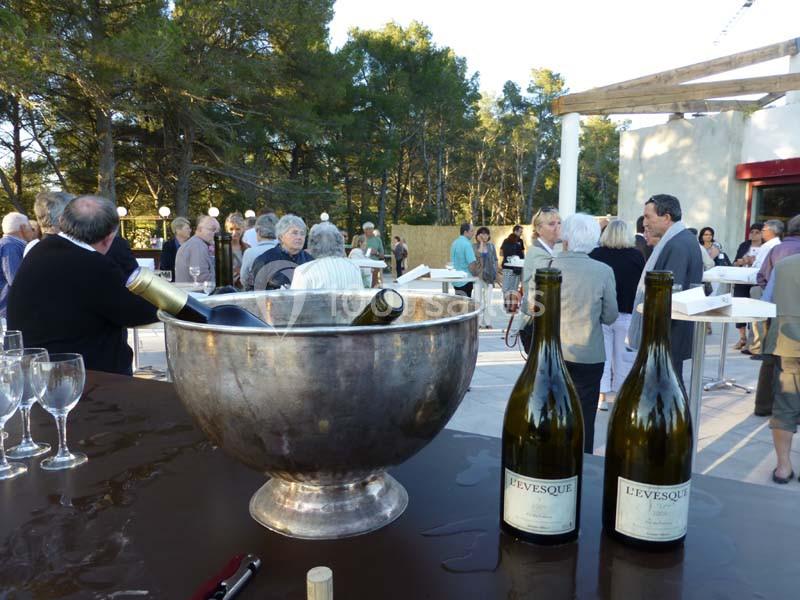 Des bouteilles de vin et un seau à glace sur une table lors d'un événement en extérieur avec des invités en arrière-plan.