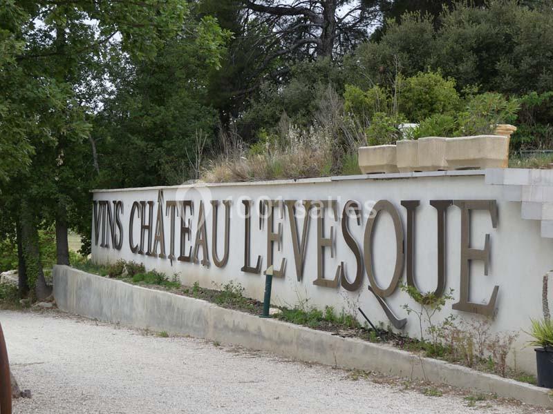 Mur avec l'inscription ’Vins Château L'Évesque’ entouré de végétation et d'un chemin en gravier.