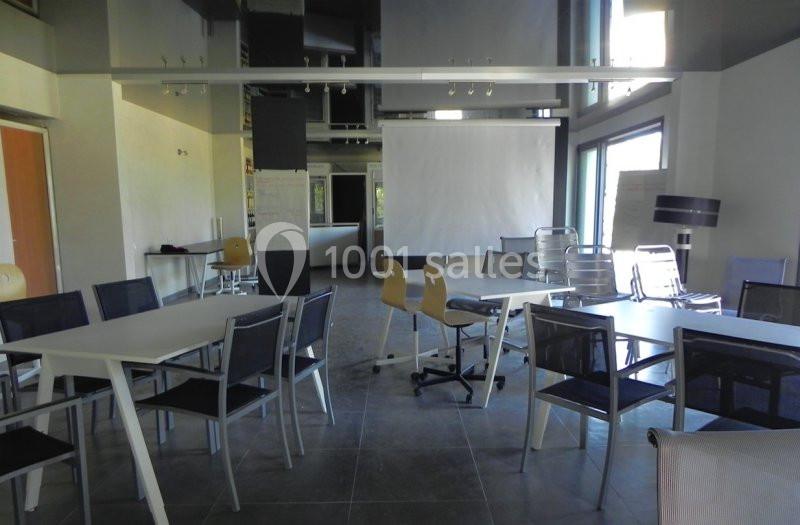 Salle de réunion lumineuse avec tables, chaises modernes et un écran de projection.