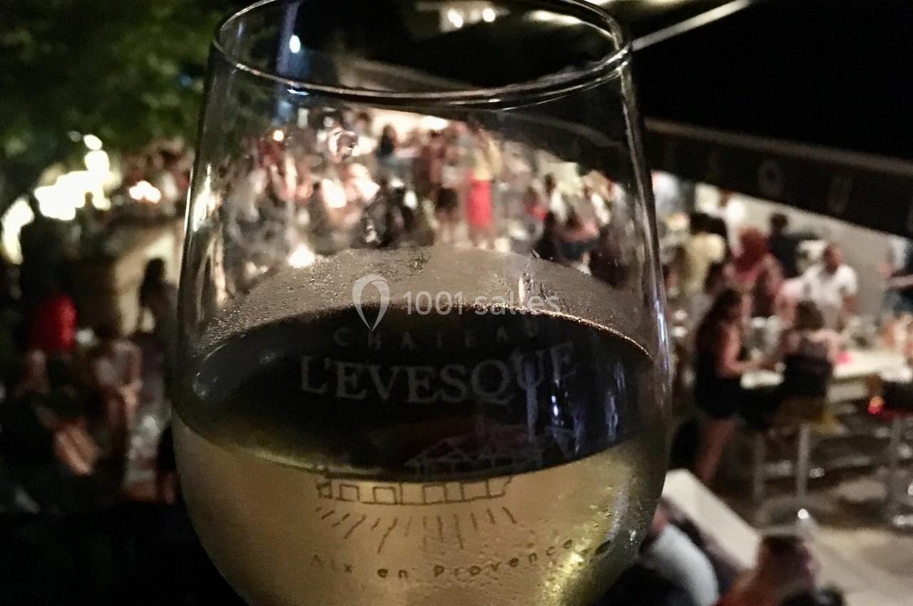 Verre de vin blanc tenu devant une scène animée en soirée, avec des personnes attablées en arrière-plan.