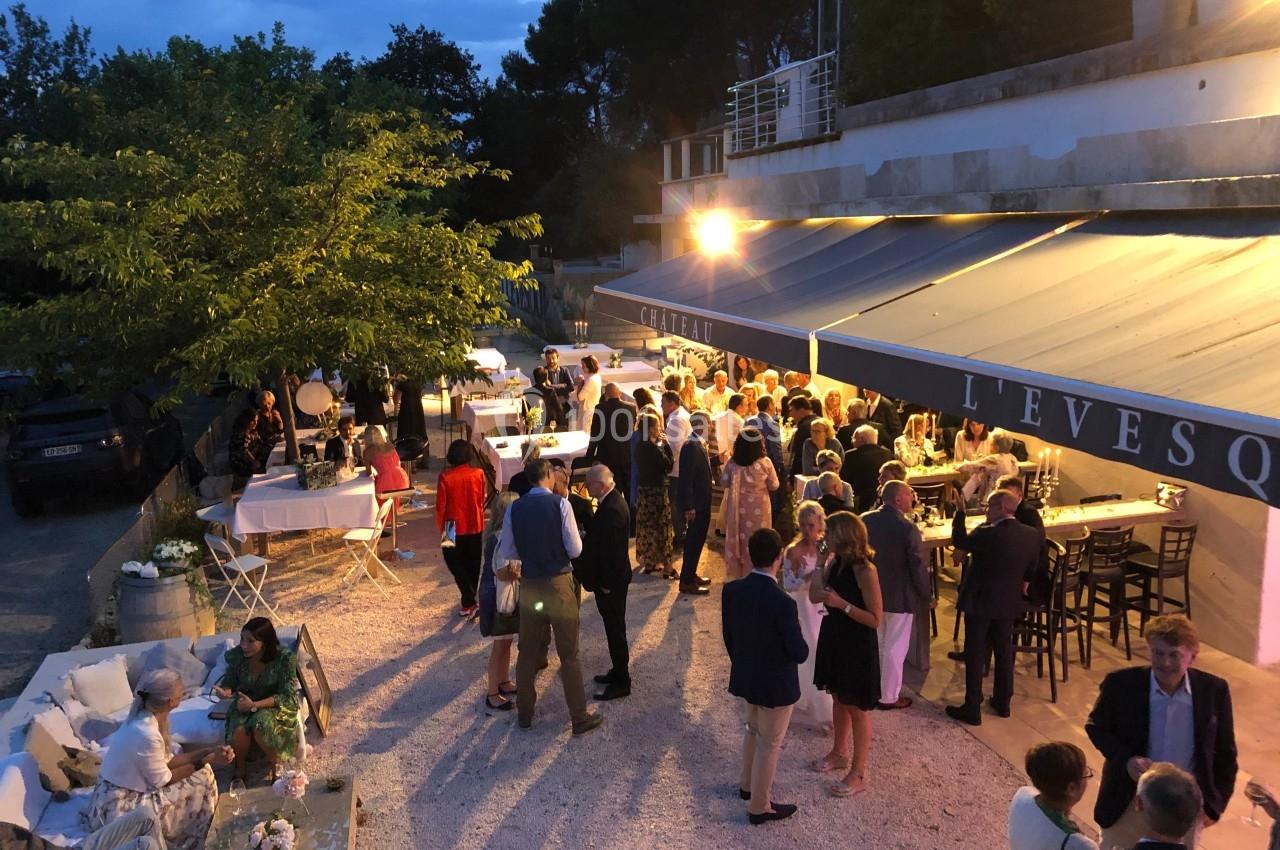 Groupe de personnes réunies en soirée en extérieur, près de tables et d'un bâtiment éclairé.