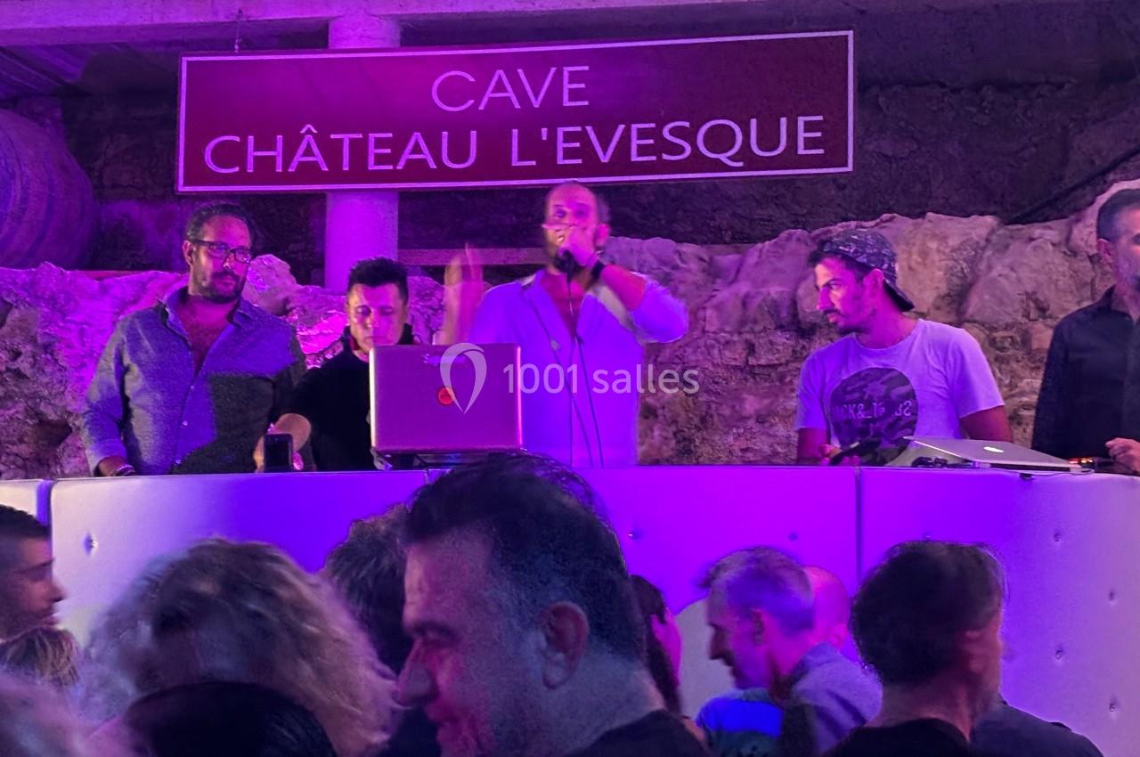 Un groupe de DJ anime une soirée dans une cave éclairée en violet, avec un public en arrière-plan.