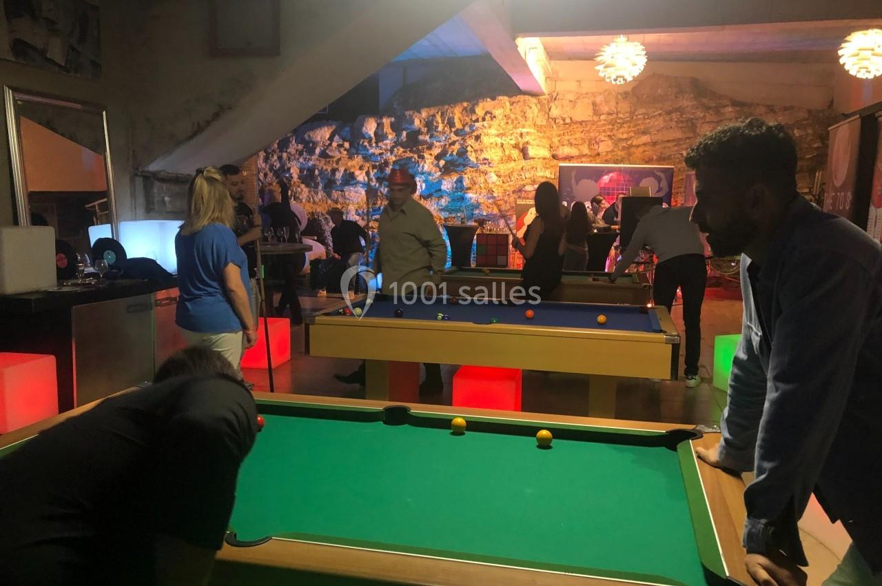 Des personnes jouent au billard dans une salle éclairée, avec plusieurs tables et une ambiance conviviale.