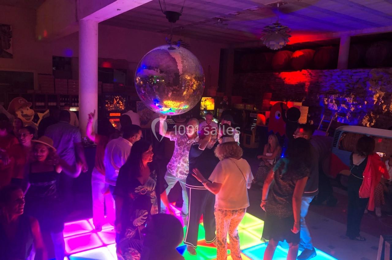 Des personnes dansent sur une piste lumineuse colorée sous une boule à facettes dans une ambiance festive.