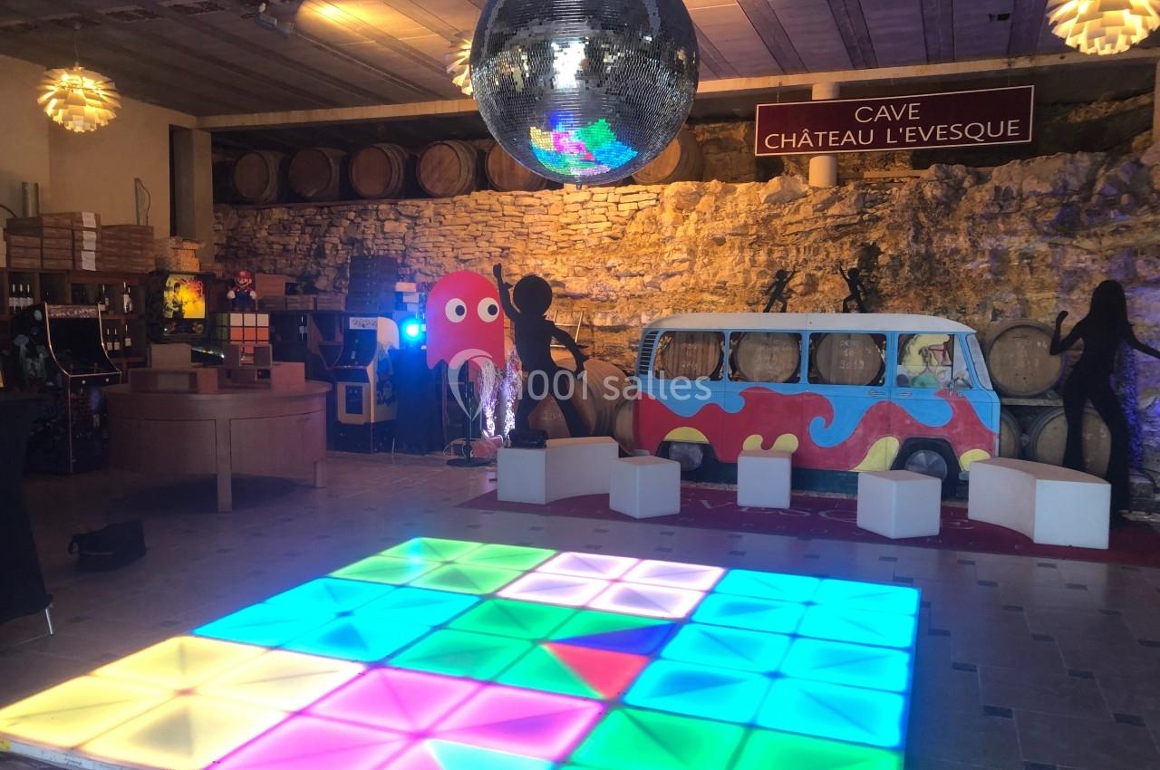 Salle décorée avec une piste de danse lumineuse, un van coloré, une boule disco et des tonneaux en arrière-plan.