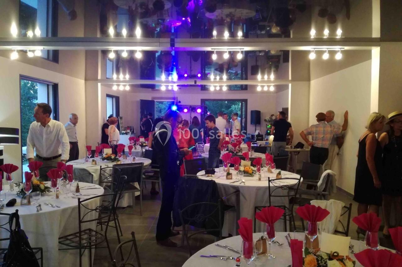 Salle de réception décorée avec des tables dressées, des invités debout discutant et des lumières colorées en arrière-plan.