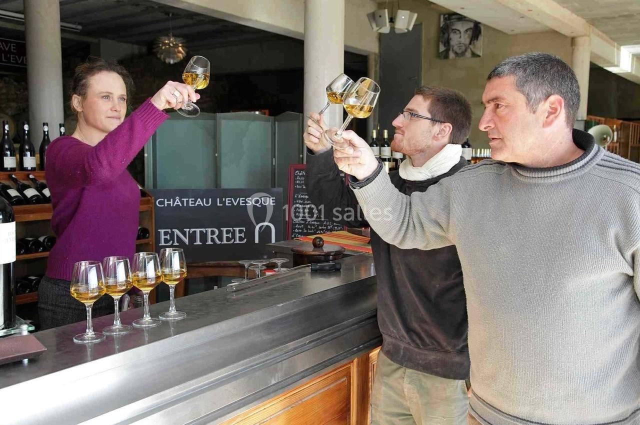Trois personnes dégustent du vin blanc dans un domaine viticole, observant la couleur des verres.
