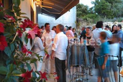Groupe de personnes discutant sur une terrasse extérieure, entourée de fleurs et de mobilier de jardin.
