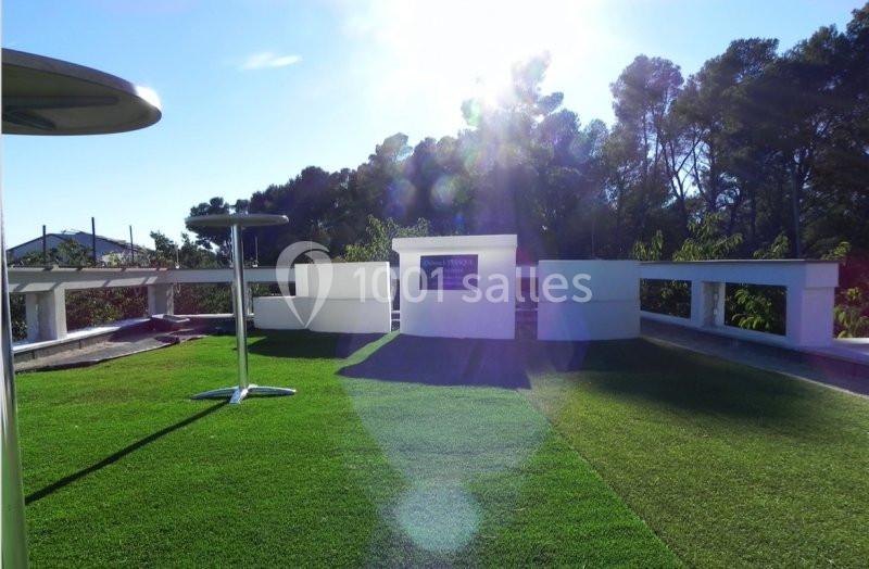 Pelouse verte sur un toit-terrasse avec structures blanches modernes, entourée d'arbres sous un ciel ensoleillé.