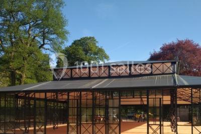 Bâtiment en verre entouré de végétation, avec des arbres et des rochers sous un ciel bleu dégagé.