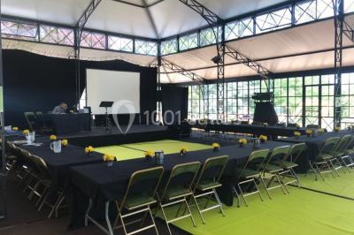 Bâtiment en verre entouré de végétation, avec des arbres et des rochers sous un ciel bleu dégagé.