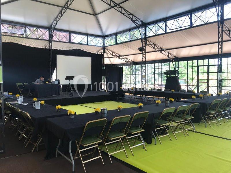 Salle de conférence lumineuse avec tables disposées en U, chaises pliantes et écran de projection à l'avant.
