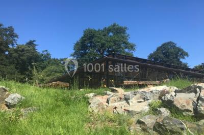 Bâtiment en verre entouré de végétation, avec des arbres et des rochers sous un ciel bleu dégagé.