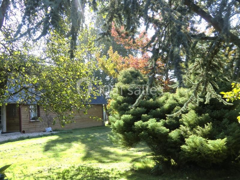 Cabane en bois entourée d'arbres et de buissons dans un jardin ensoleillé.