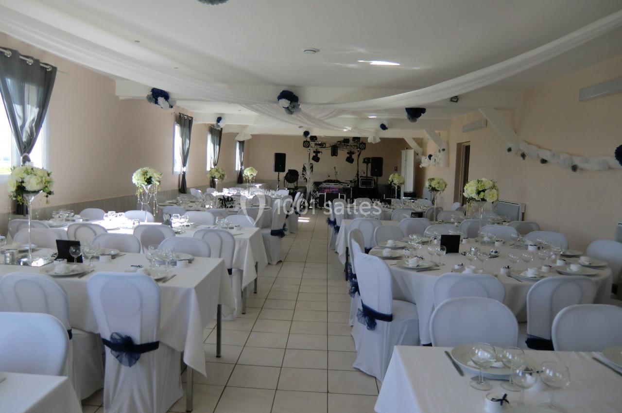 Salle de réception décorée avec des tables dressées, des chaises blanches et des fleurs, prête pour un événement.