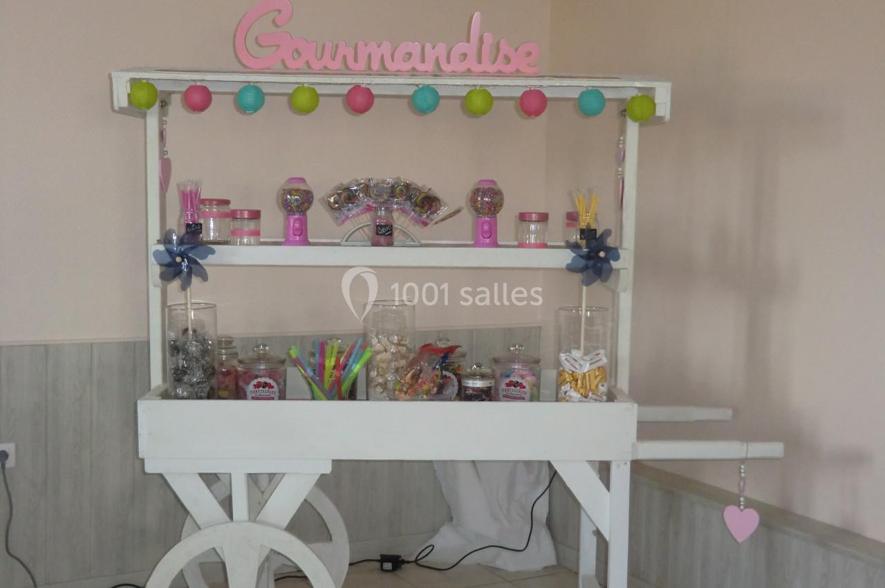 Chariot en bois blanc décoré, rempli de bonbons colorés dans des bocaux, avec une enseigne ’Gourmandise’.