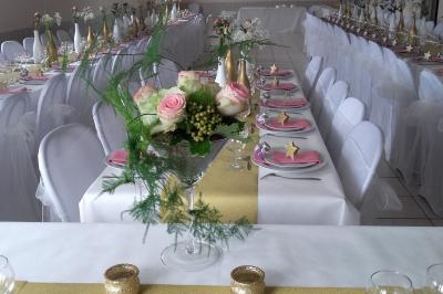 Table élégamment dressée avec nappes blanches, bougies, fleurs, verres et petits pains alignés.