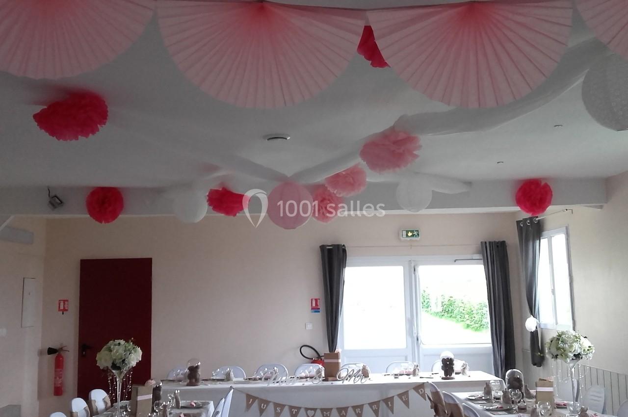 Décoration de salle avec des lanternes et pompons roses et blancs suspendus, table dressée en arrière-plan.