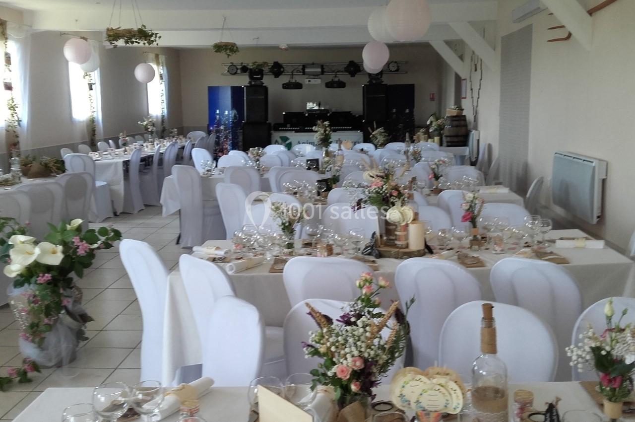 Salle de réception décorée pour un événement, avec des tables dressées, nappes blanches et arrangements floraux.