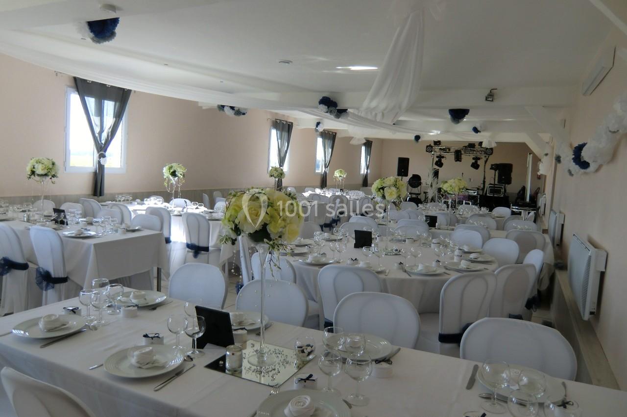 Salle de réception décorée pour un événement, avec tables dressées, nappes blanches et arrangements floraux.