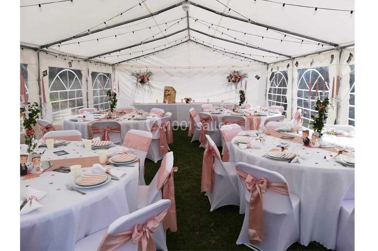 Salle de réception sous chapiteau blanc, décorée de nappes blanches et rubans roses, avec tables dressées pour un événement.