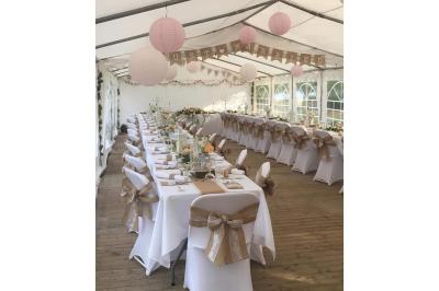 Table élégamment dressée avec nappes blanches, bougies, fleurs, verres et petits pains alignés.