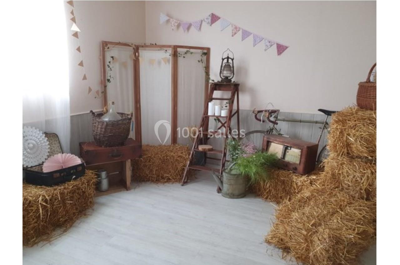 Décoration champêtre avec bottes de paille, échelle en bois, objets vintage et guirlandes dans une pièce lumineuse.