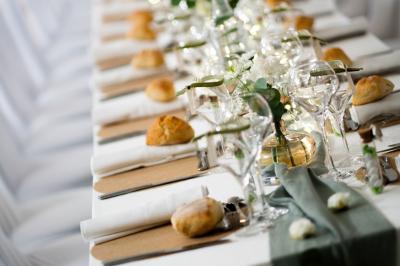 Table élégamment dressée avec nappes blanches, bougies, fleurs, verres et petits pains alignés.