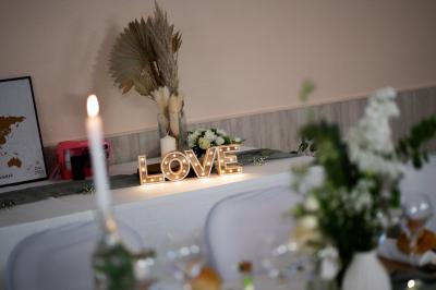 Table élégamment dressée avec nappes blanches, bougies, fleurs, verres et petits pains alignés.