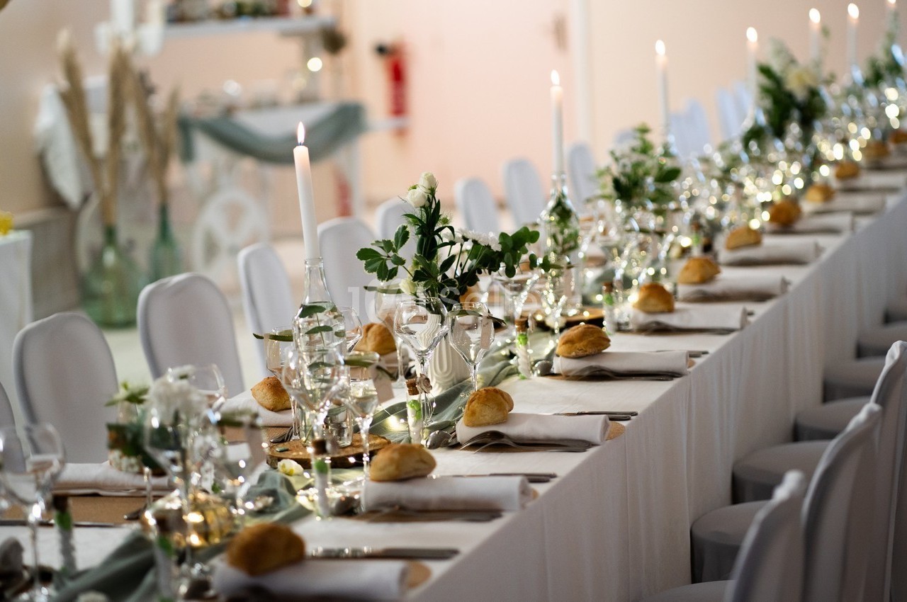 Table de réception élégamment dressée avec nappes blanches, bougies, fleurs et pains individuels.