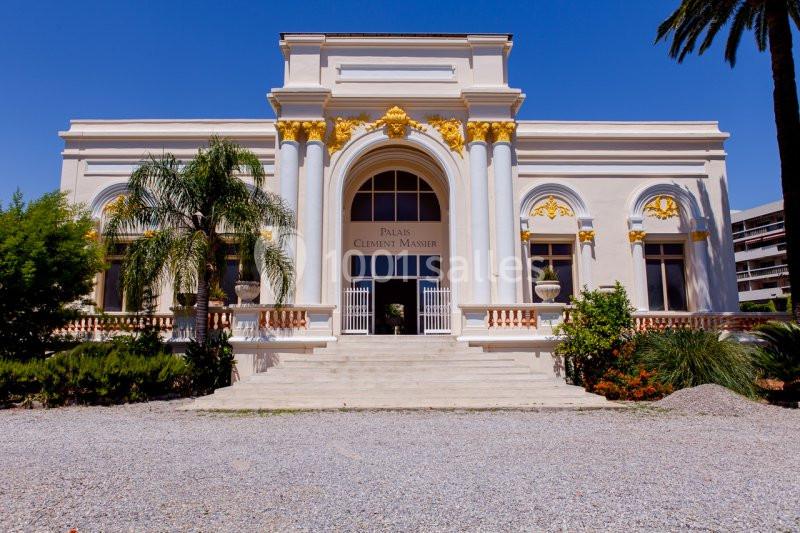 Façade d'un bâtiment blanc de style classique avec colonnes, ornements dorés et palmiers à proximité.