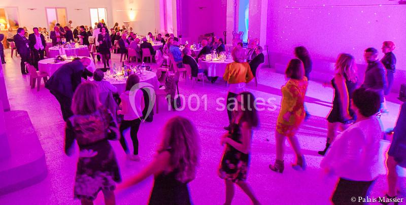 Salle de réception éclairée en violet avec des invités dînant à table et d'autres dansant au premier plan.