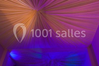 Piscine extérieure entourée de tables hautes, chaises colorées et structures gonflables, avec colline en arrière-plan.