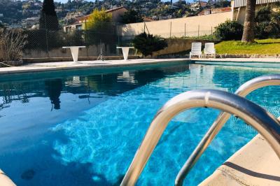 Piscine extérieure entourée de tables hautes, chaises colorées et structures gonflables, avec colline en arrière-plan.