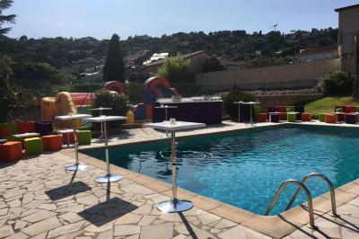 Piscine extérieure entourée de tables hautes, chaises colorées et structures gonflables, avec colline en arrière-plan.